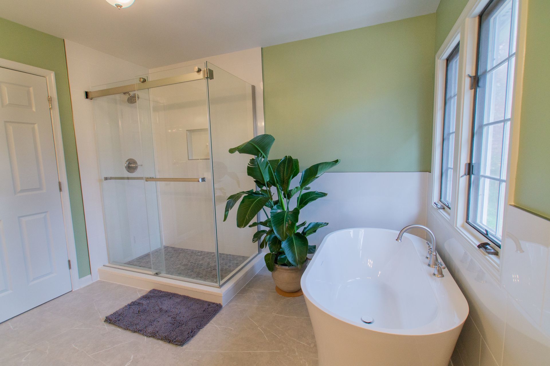 Bathroom with a glass shower, a freestanding tub, and a large potted plant, featuring green walls.