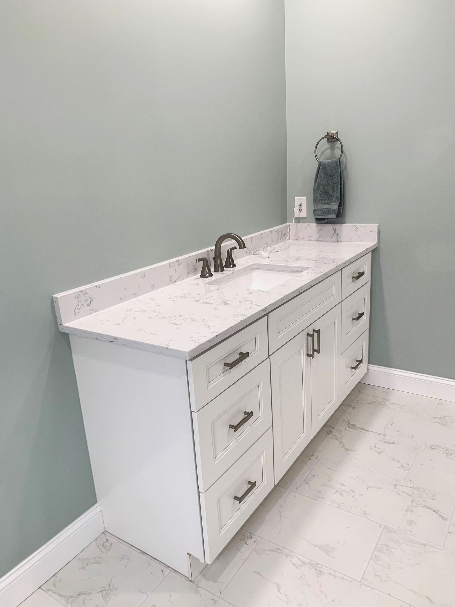 White bathroom vanity with marble countertop and chrome faucet, in a corner with a wall-mounted towel ring and a green towel.