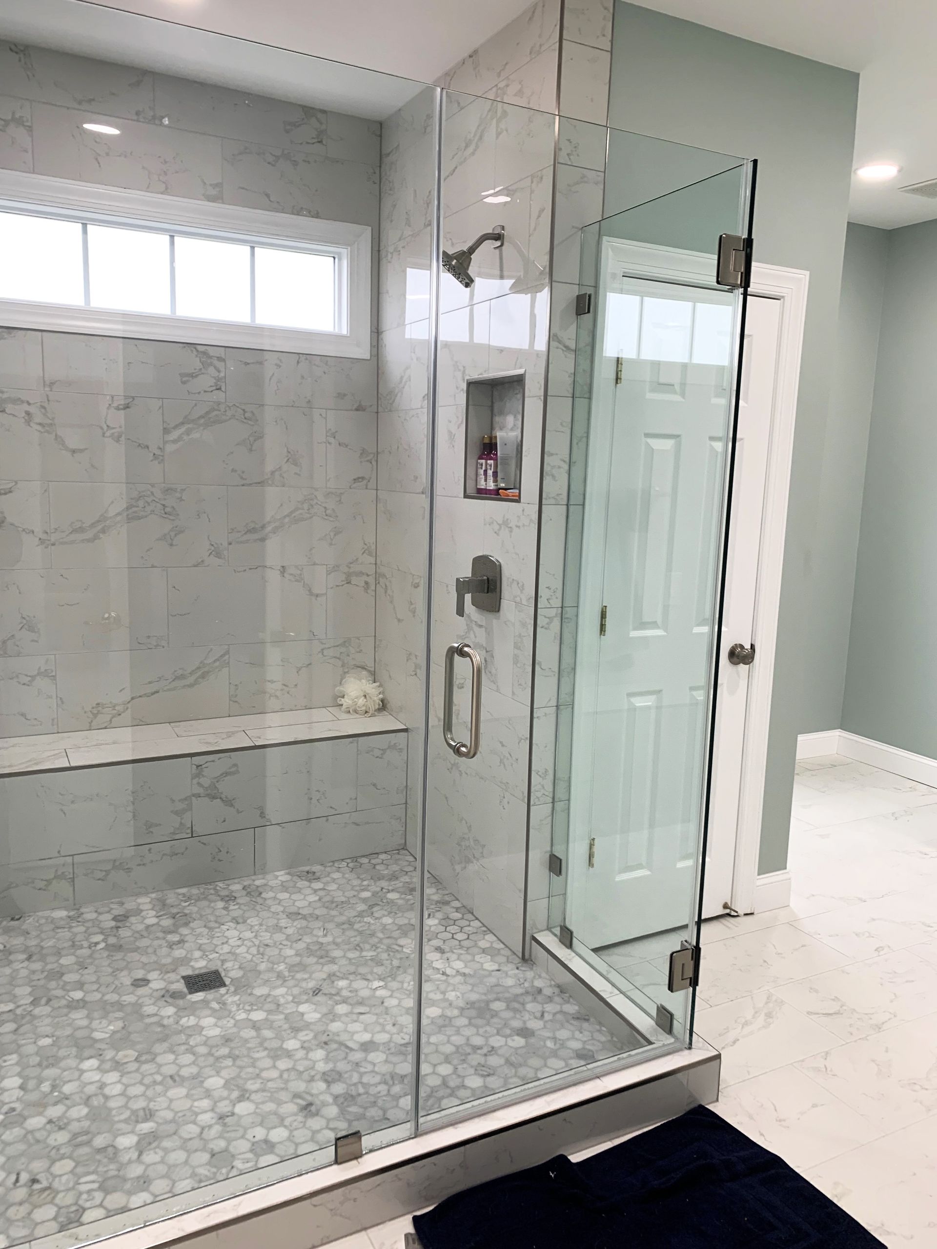 Modern bathroom with a glass shower enclosure, marble-tiled walls and floor, and a built-in bench.