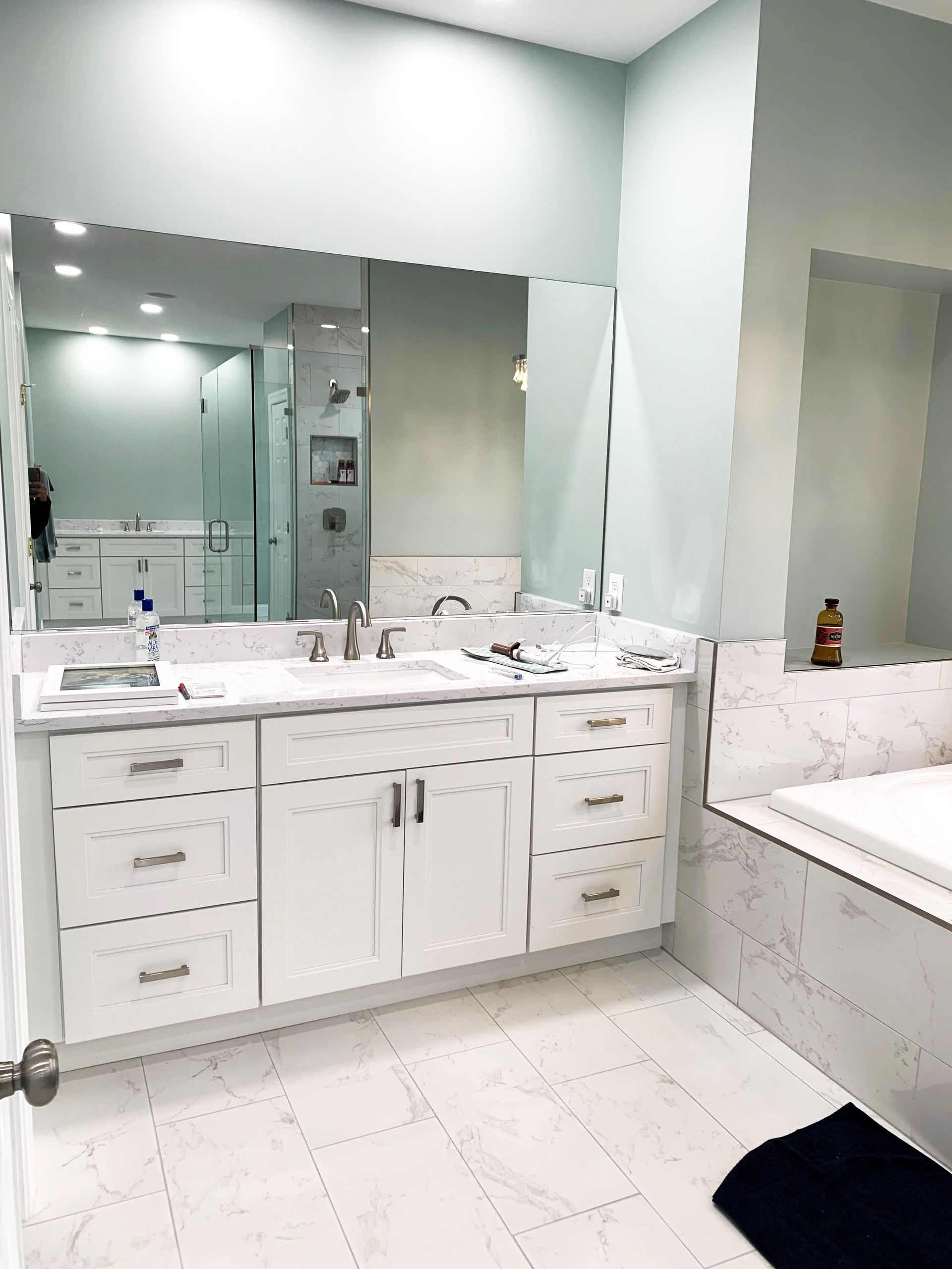 White bathroom with a vanity, large mirror, and tub. The walls are a light green, and the floor has white tiles.