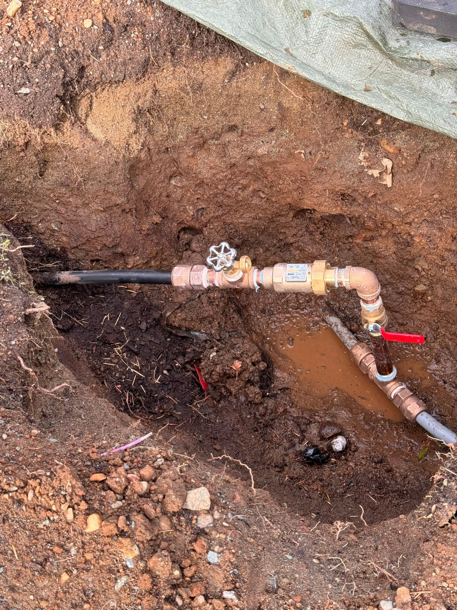 A water pipe is sitting in the dirt in a hole.