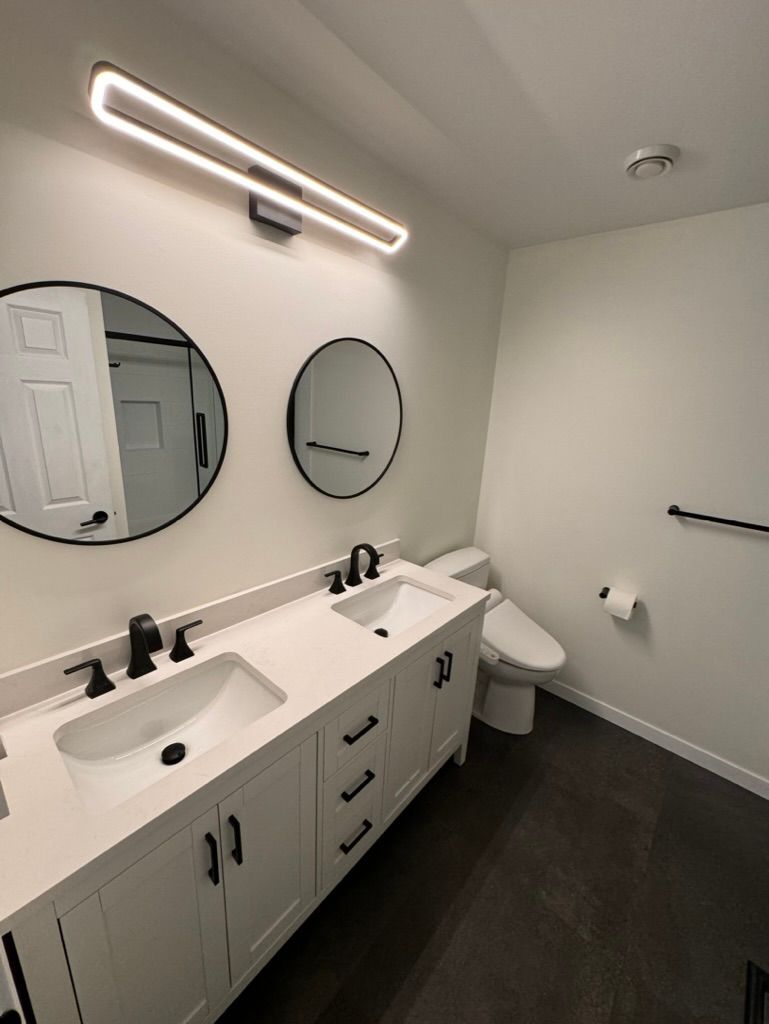 A bathroom with two sinks , a toilet , and two mirrors.