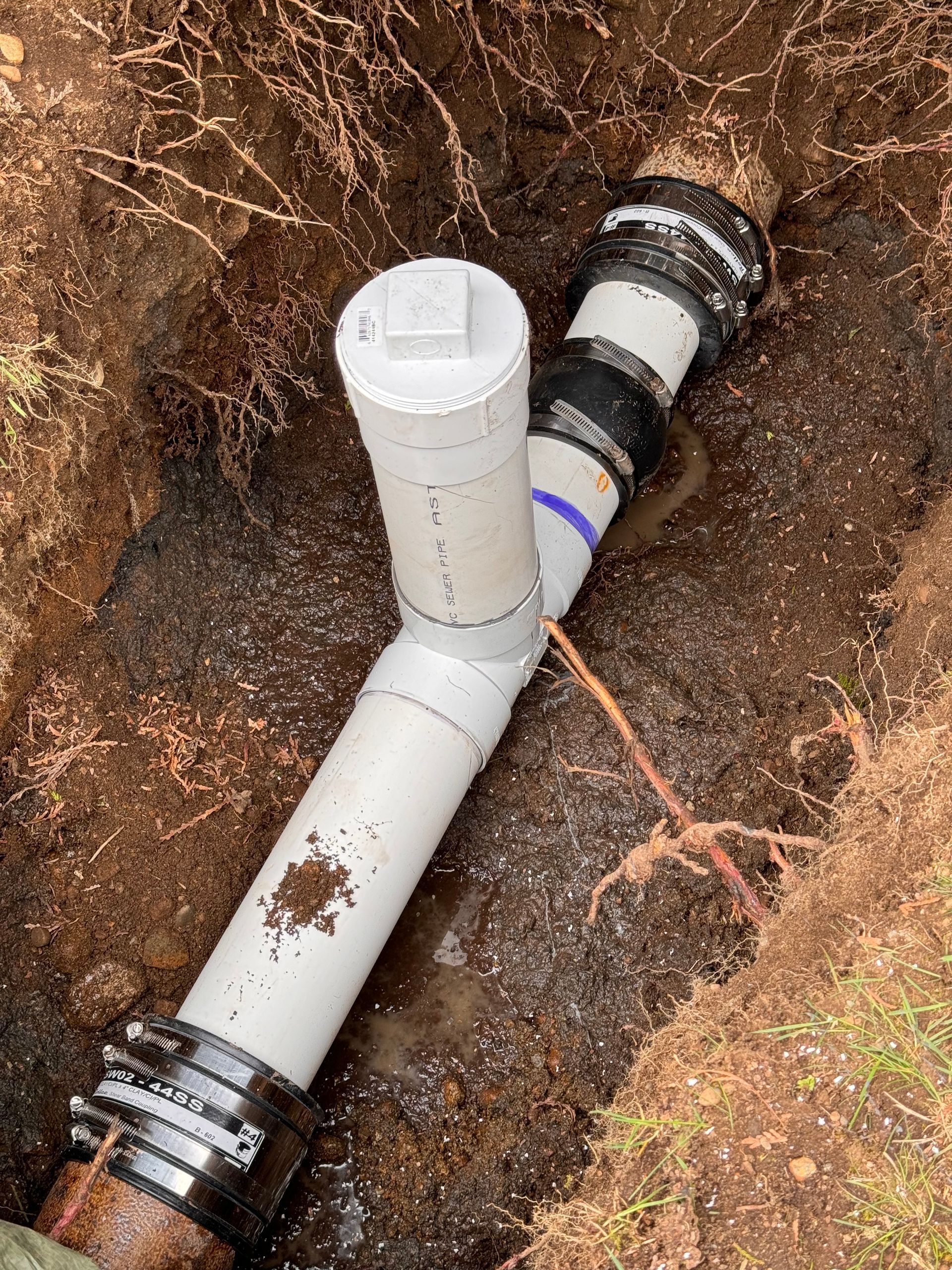 A white pipe is laying in the dirt in a hole.