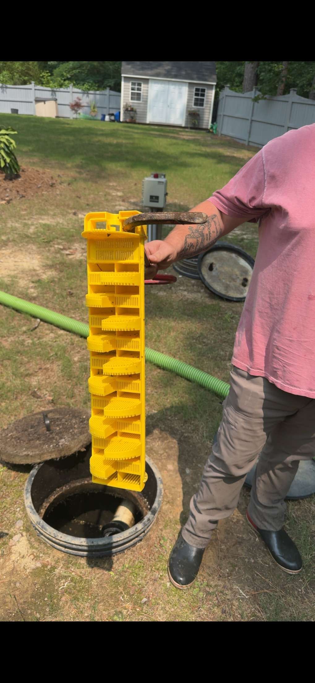 A person holding a yellow, stepped filter over a septic tank, outdoors on grass.