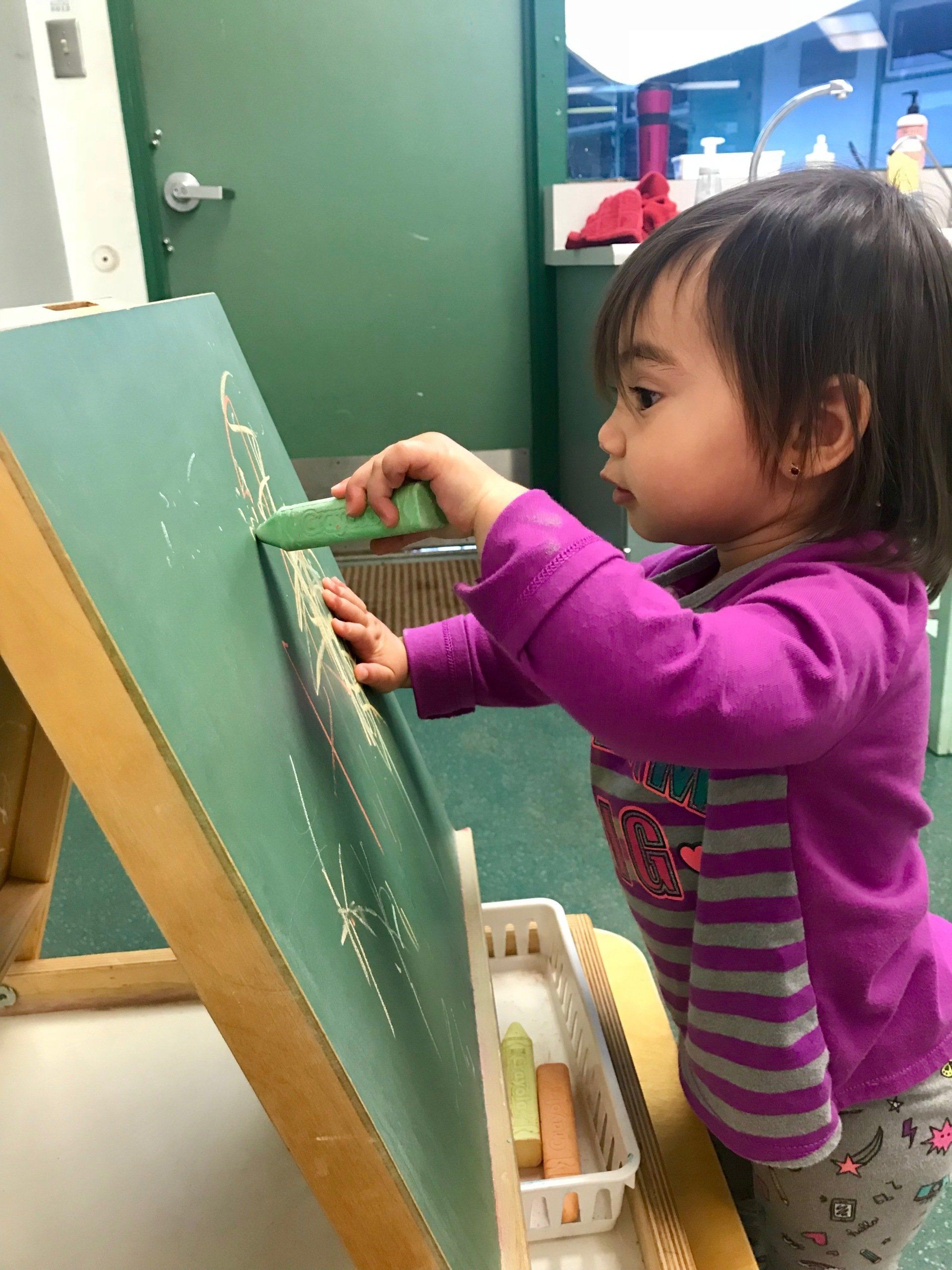 A Montessori toddler drawing on a chalkboard.