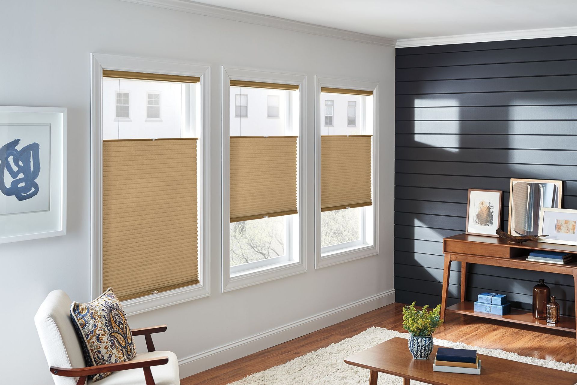 Living room with three windows featuring light brown cellular shades; a dark accent wall, and wood furniture.