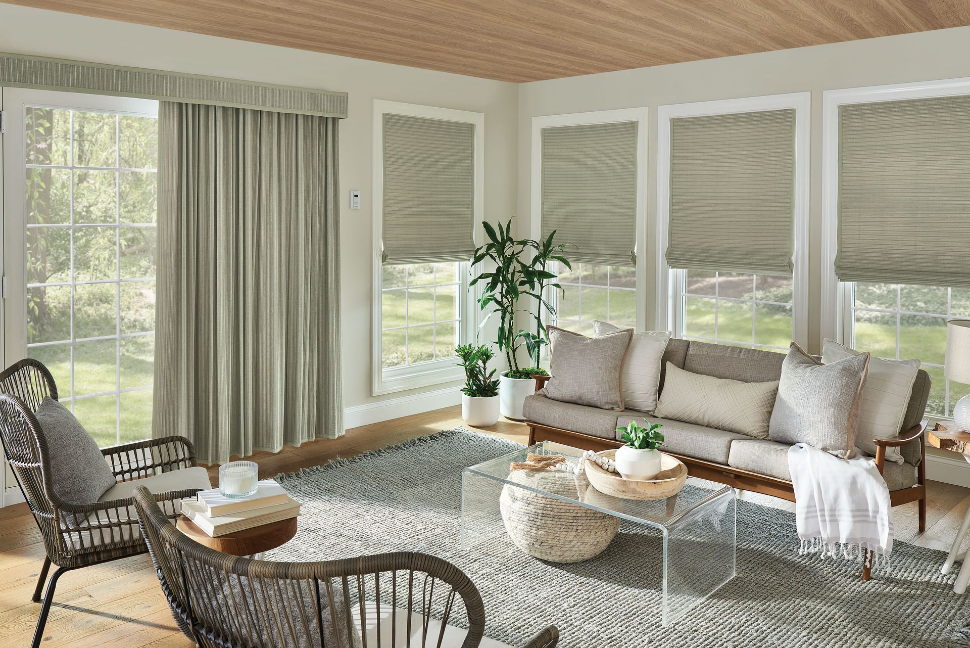 Sunroom with light gray curtains, woven chairs, sofa with pillows, and woven shades on the windows.