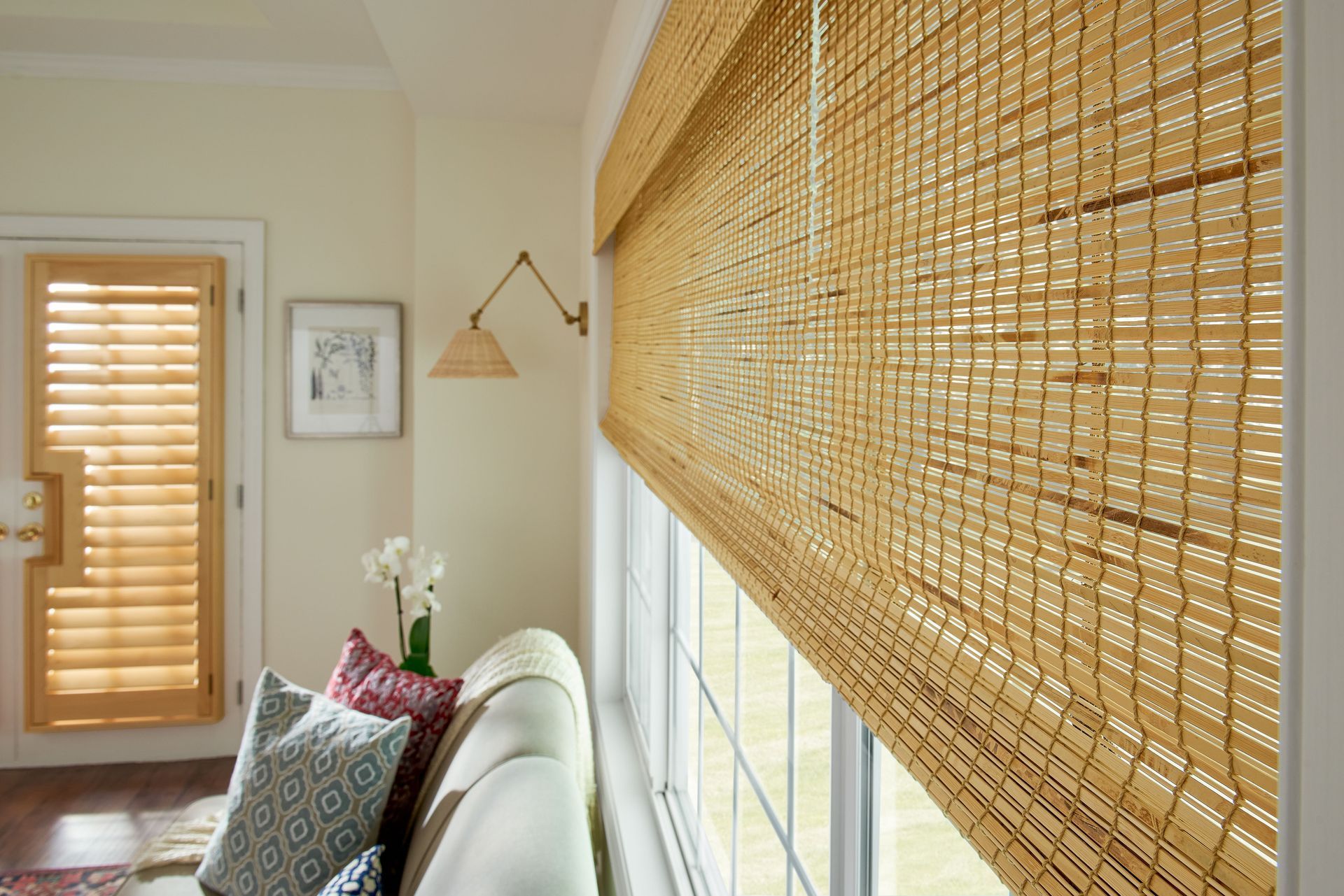 Light brown woven window shade over a window in a cream-colored room; a sofa and door are also visible.