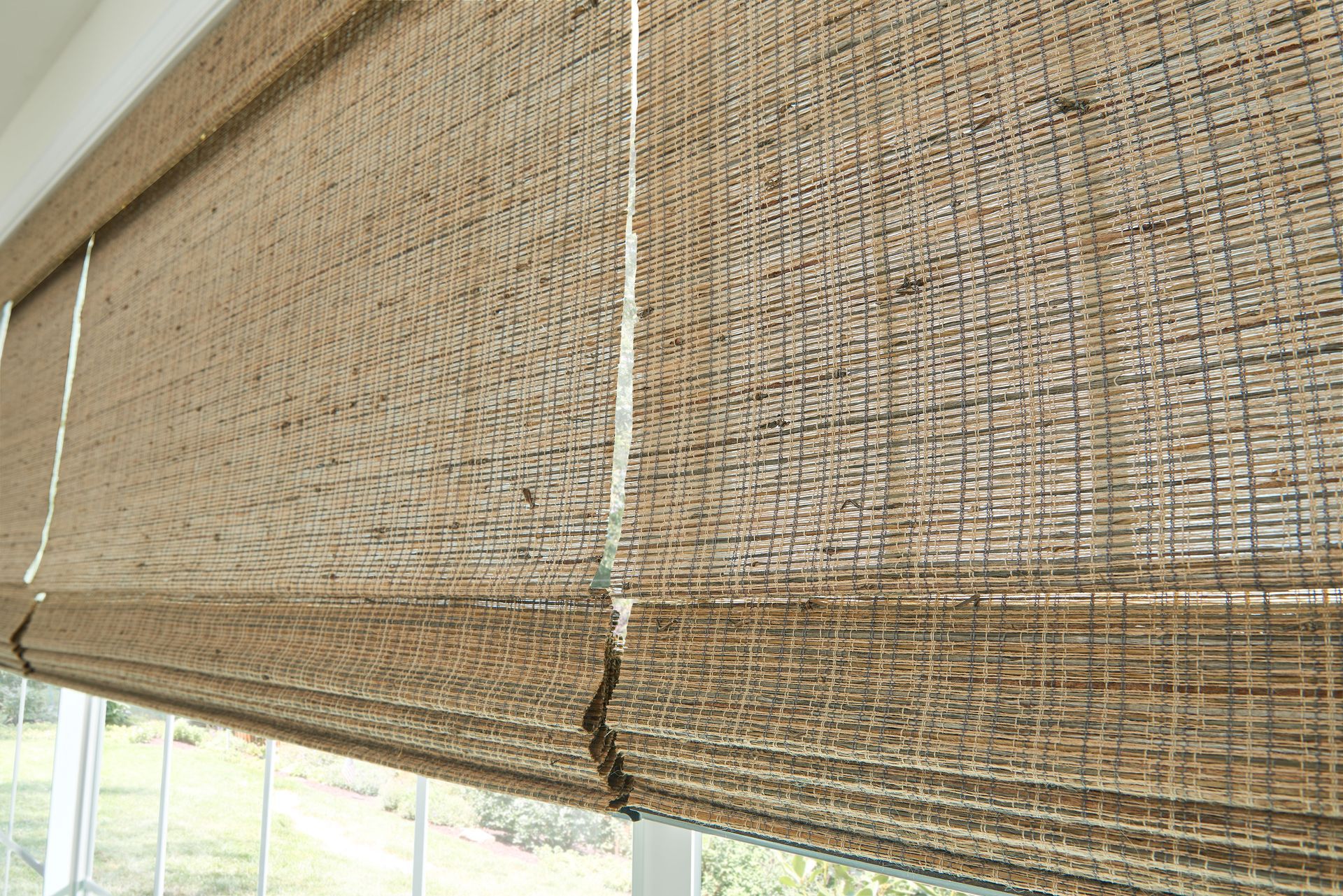 Beige woven bamboo shade partially covering a window.