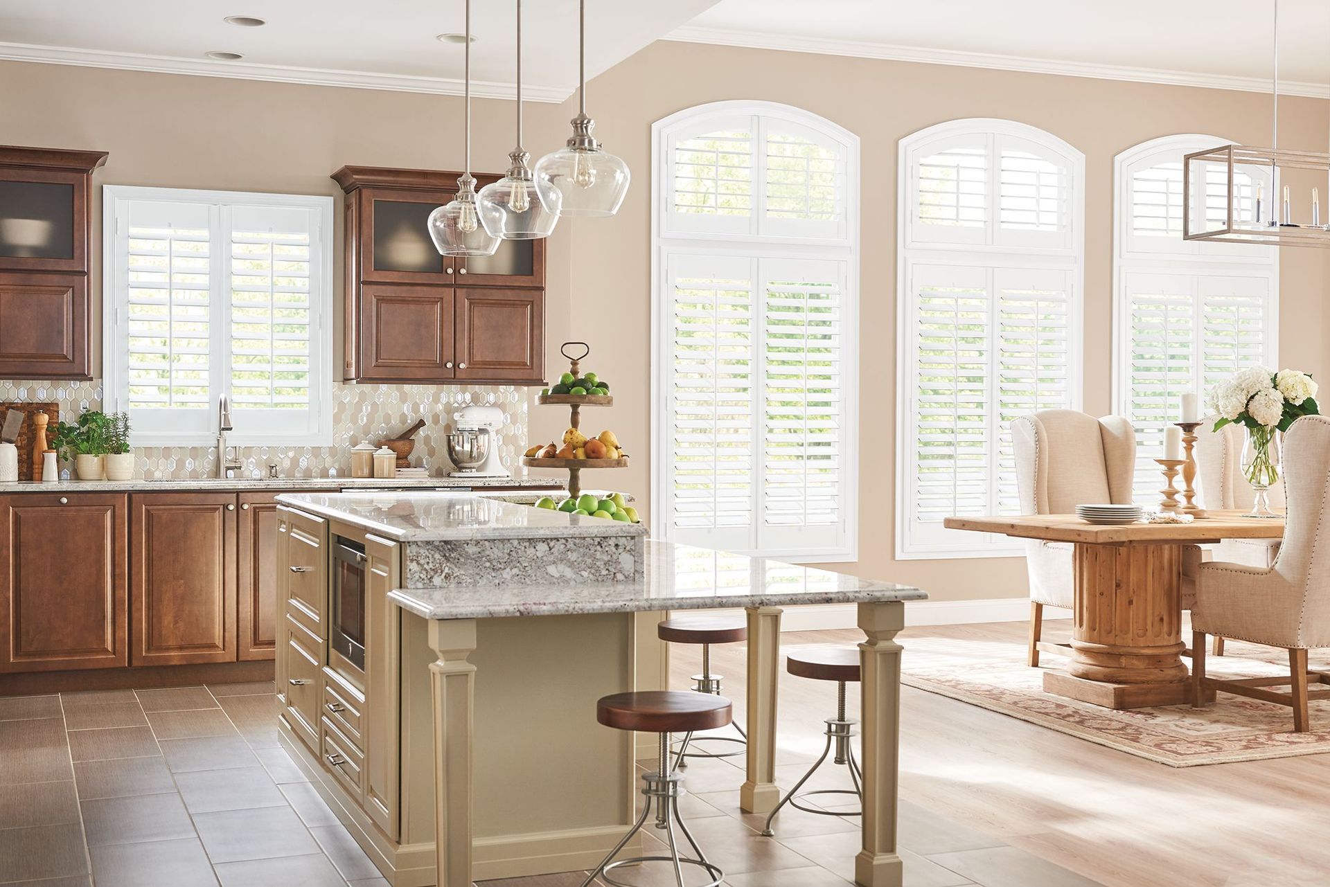 Kitchen with brown cabinets, island, granite countertop, and arched windows with white shutters.