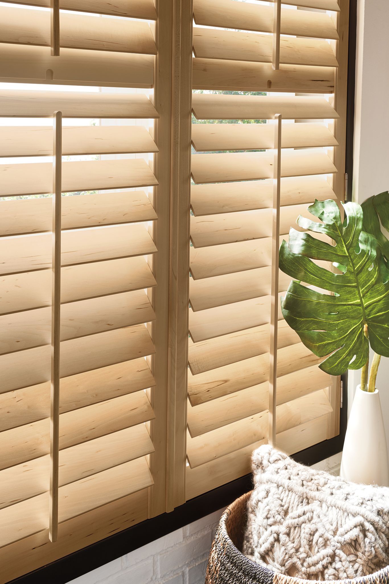 Wooden window shutters with open slats, a vase with a plant, and a decorative pillow.