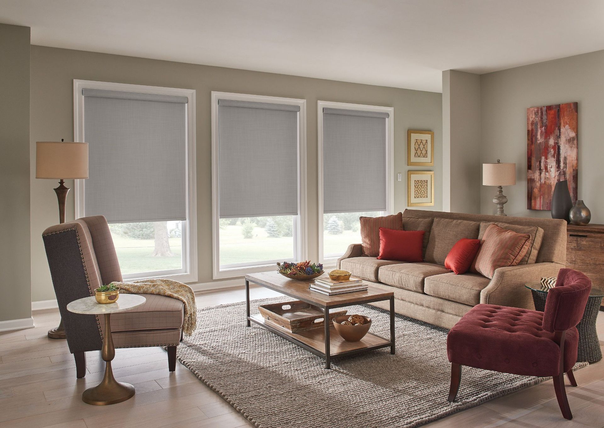 Living room with gray blinds, tan couch, armchairs, coffee table, rug, artwork.