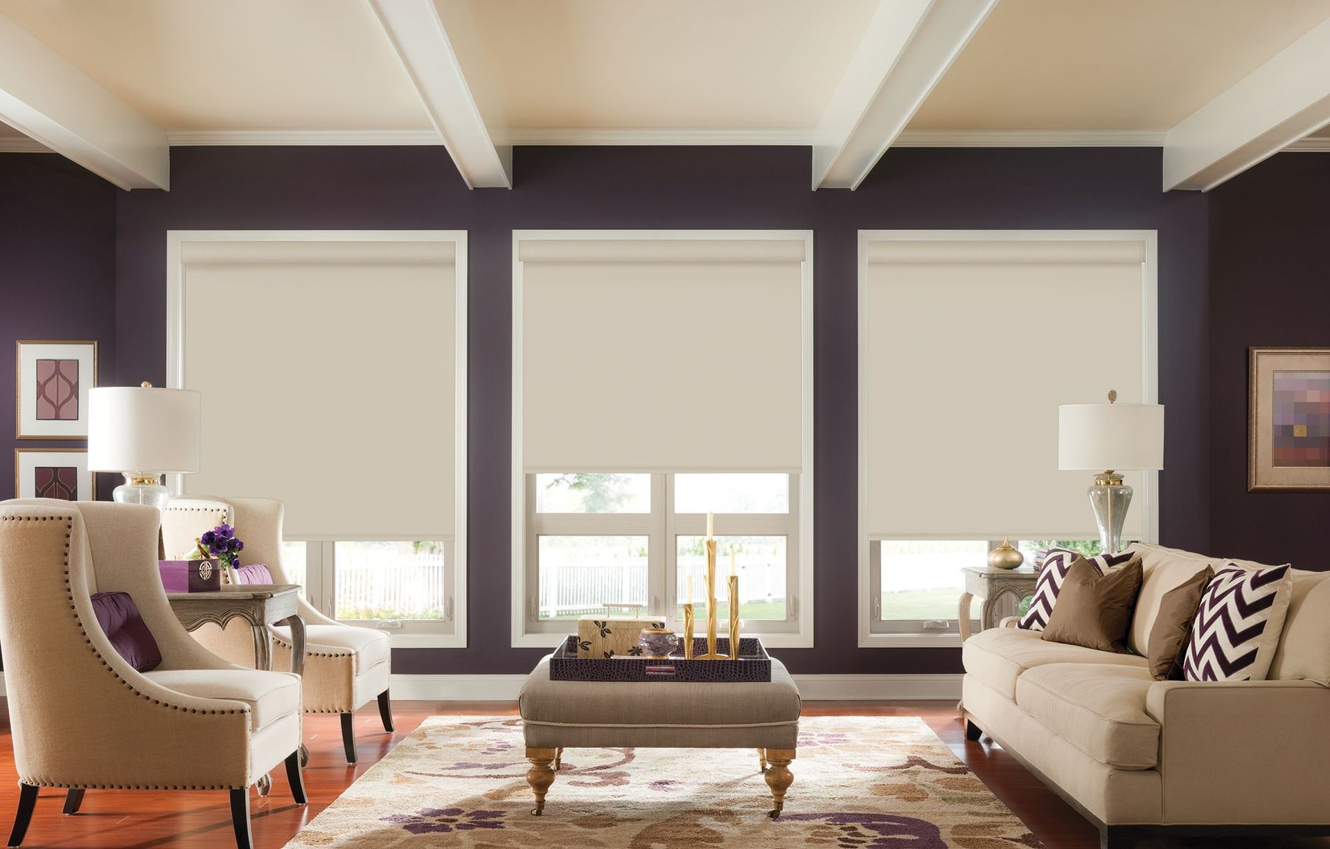 Living room with three windows covered by cream-colored roller shades, purple walls, and beige furniture.