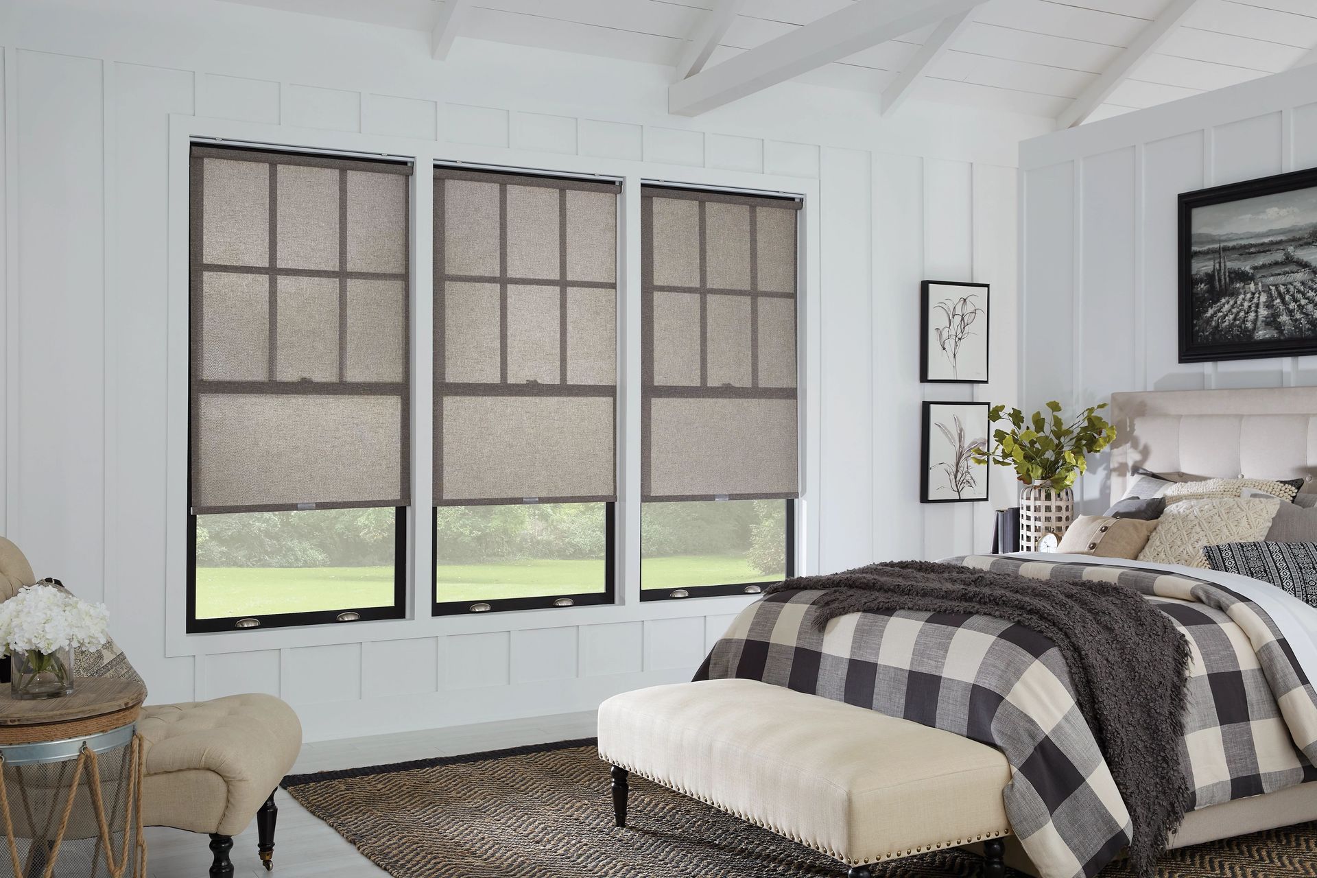 Bedroom with three windows, neutral-toned roller shades, white walls, and a plaid blanket on a bed.