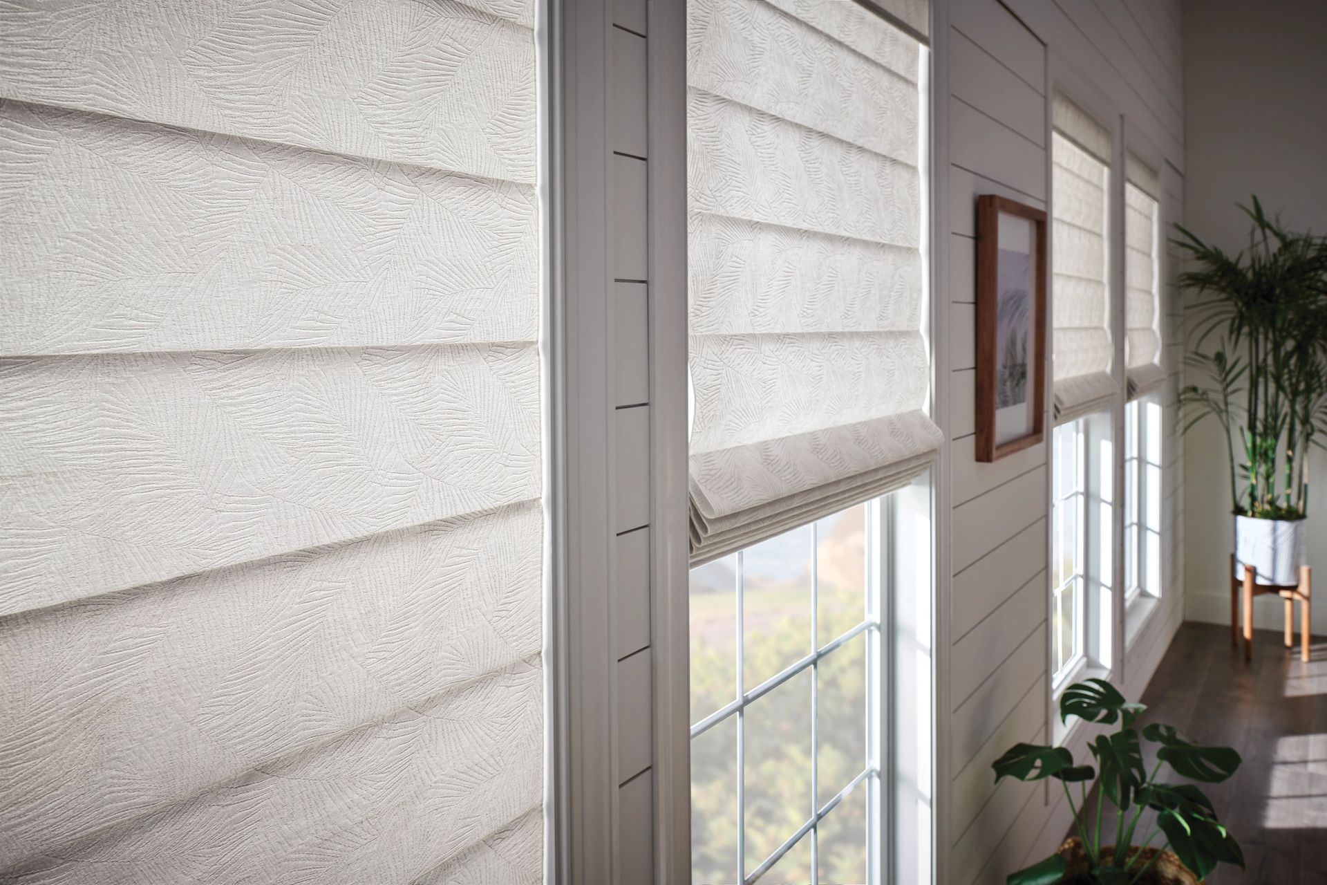 Interior view of windows with neutral-toned Roman shades and textured white siding.