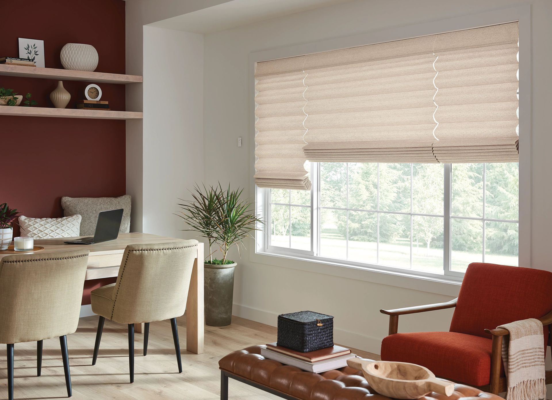 Living room with dining table, red accent wall, beige Roman shades, and an orange armchair.