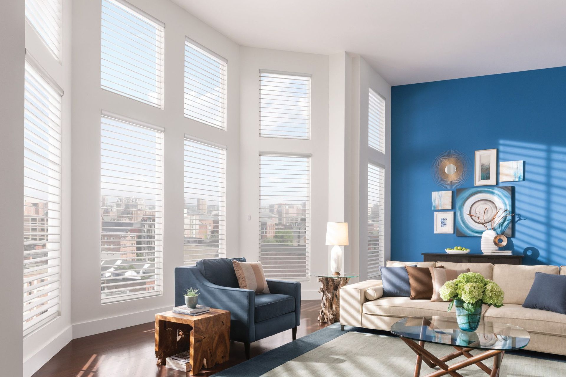 Living room with large windows, blue accent wall, neutral couch, armchair, and city view.