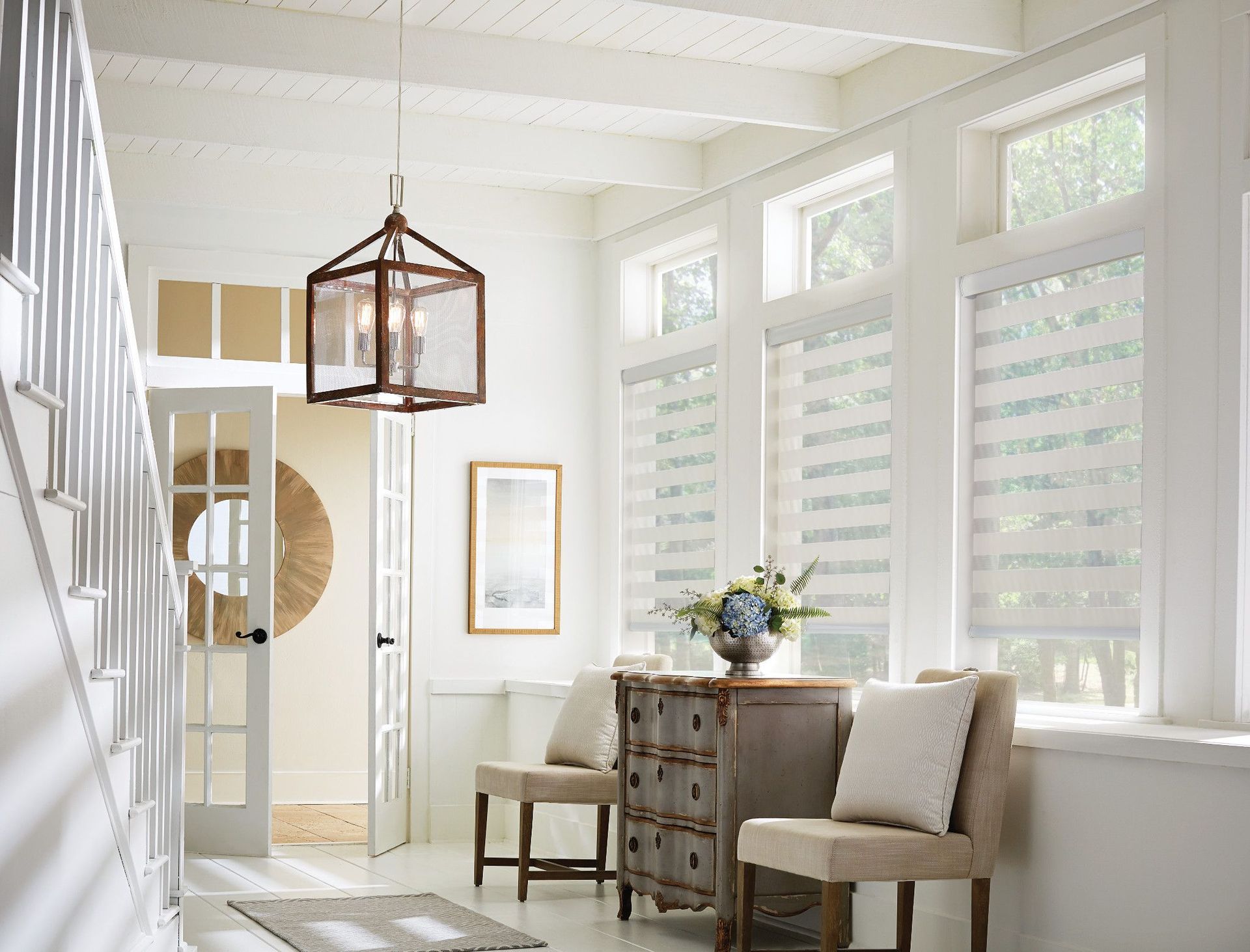 Bright hallway with white walls, windows, and furniture; a decorative light fixture hangs from the ceiling.