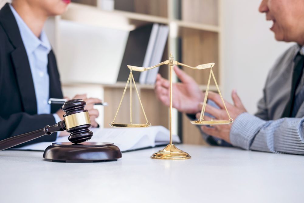 A man and a woman are sitting at a table with scales of justice and a judge 's gavel.