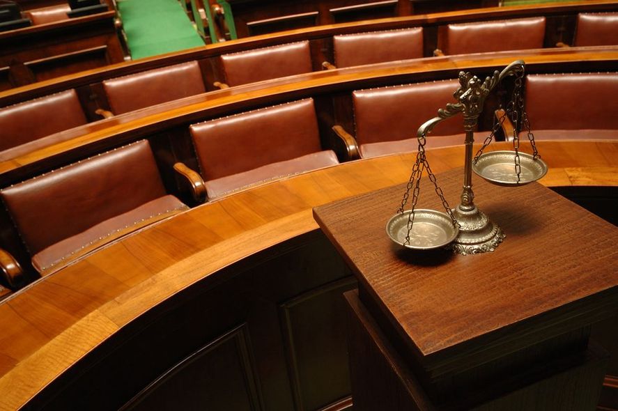 A scale of justice sits on a wooden table in a courtroom