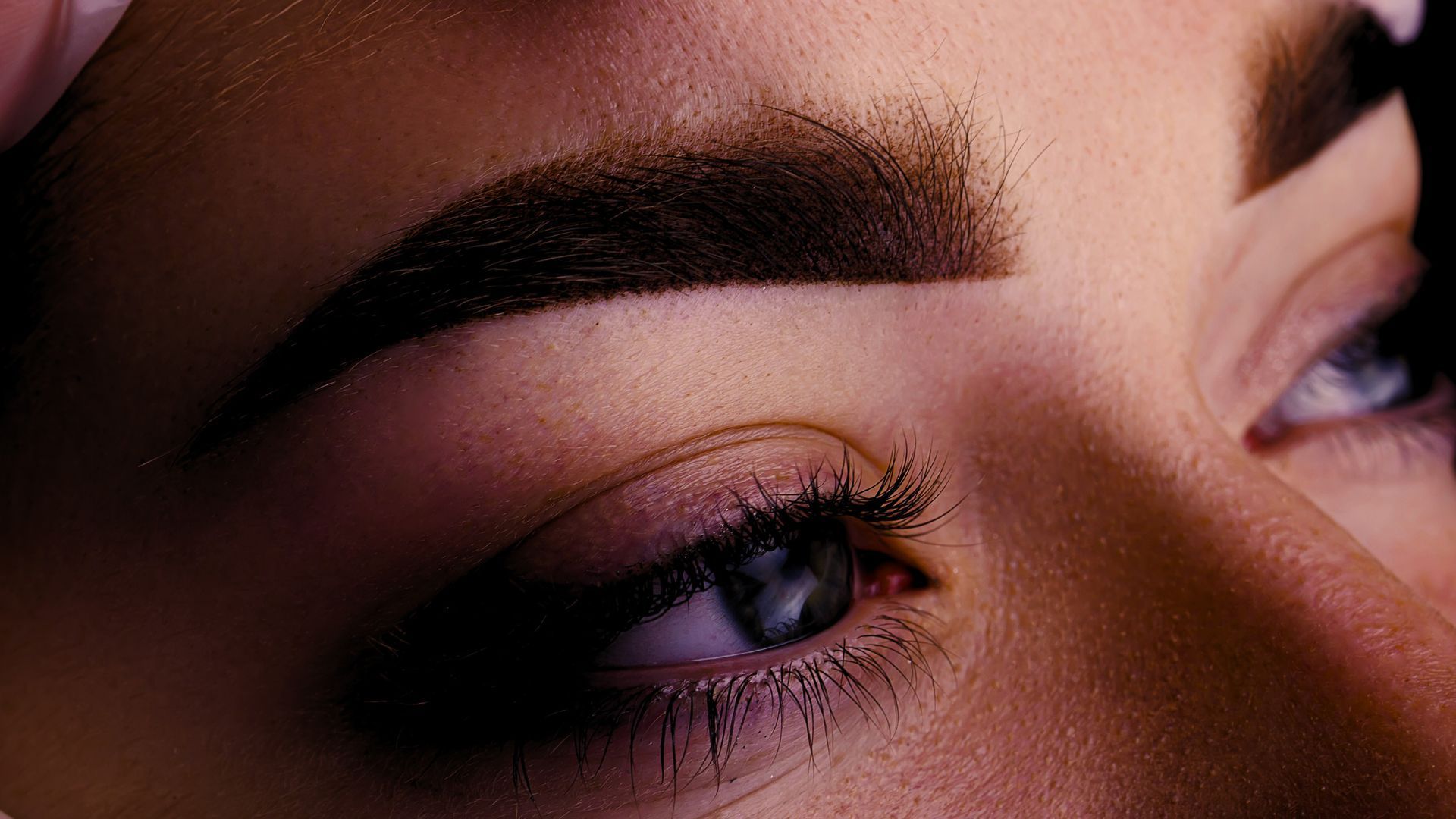 A woman is getting her eyebrows done by a makeup artist.