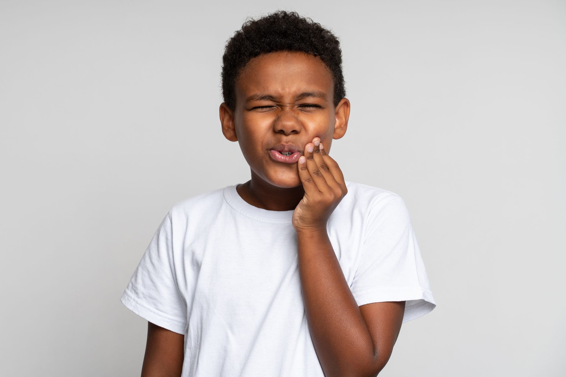 A young boy is holding his mouth in pain because of a toothache.