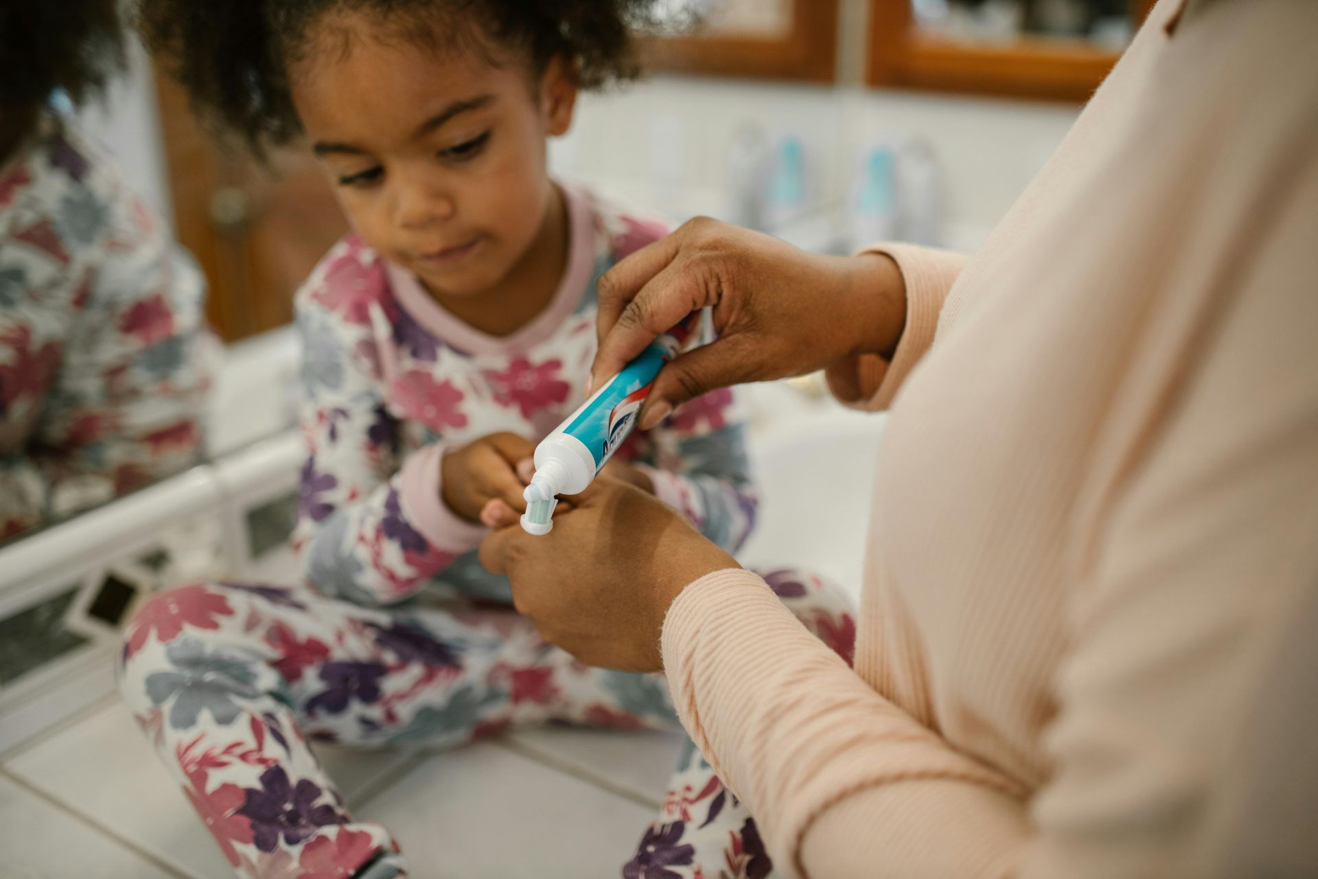 A woman is putting toothpaste on a little girl 's finger.