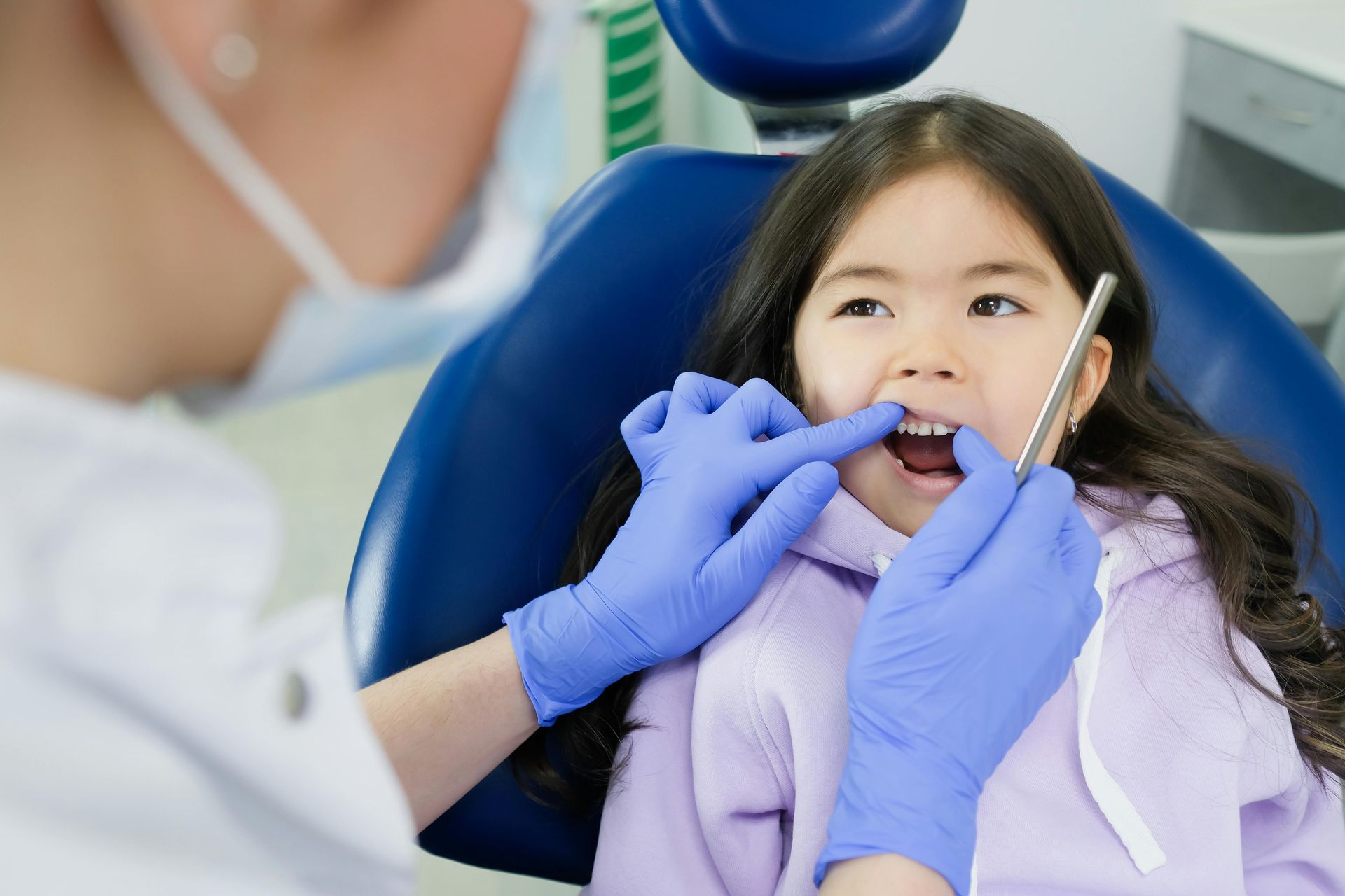 A little girl is sitting in a dental chair getting her teeth examined by a dentist.