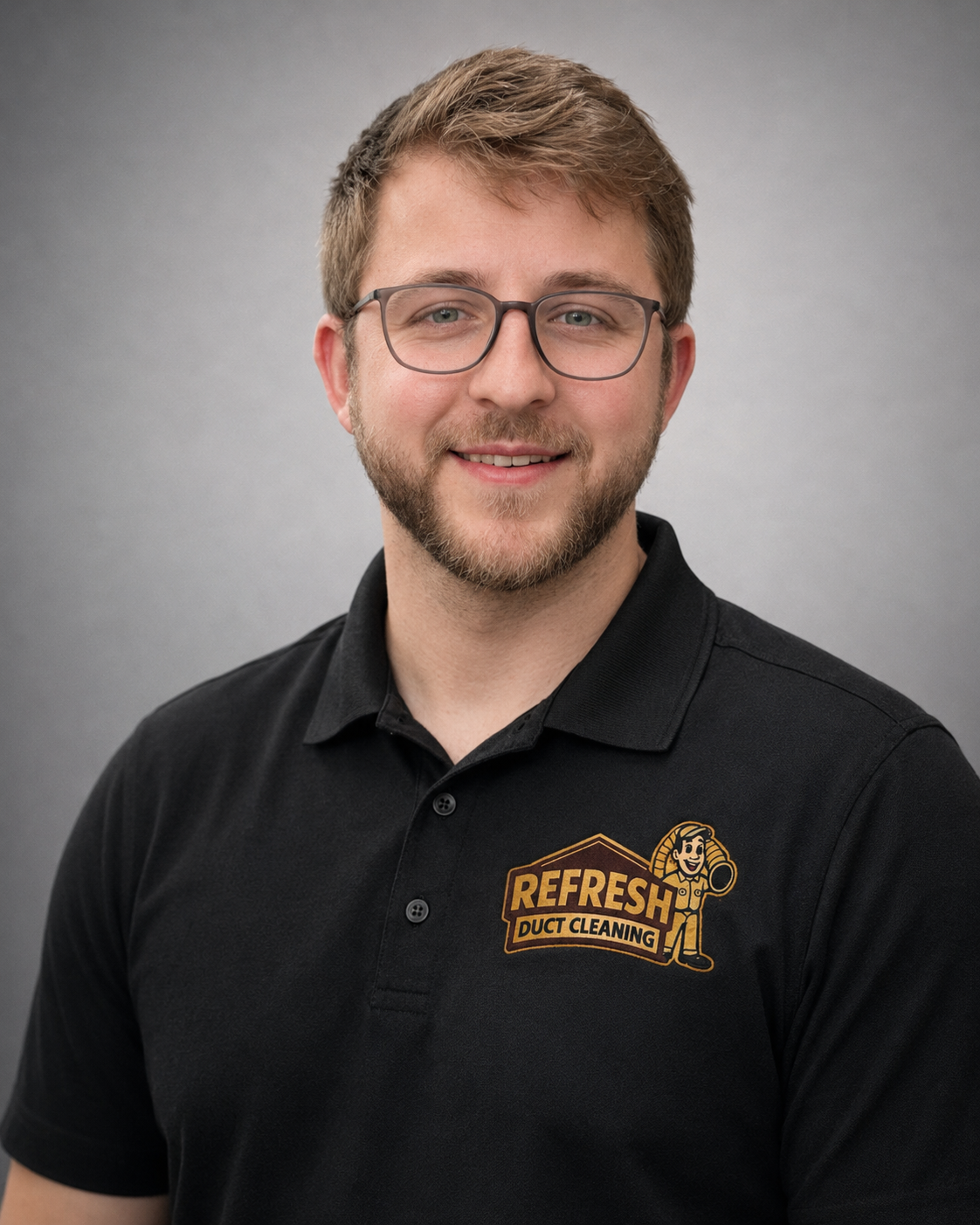 Smiling person in glasses wearing a black polo with a βRefreshβ logo on a gray background