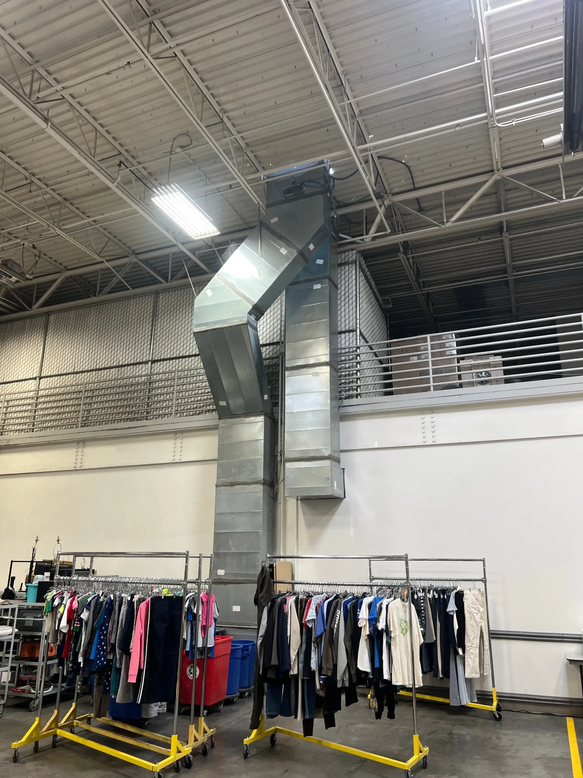 Clothing racks in a warehouse-style store under high metal ceilings and exposed ductwork