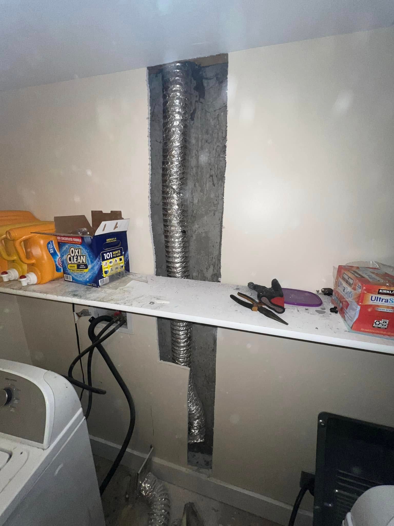 Laundry shelf with foil-covered ductwork, cleaning supplies, and tools against a wall.