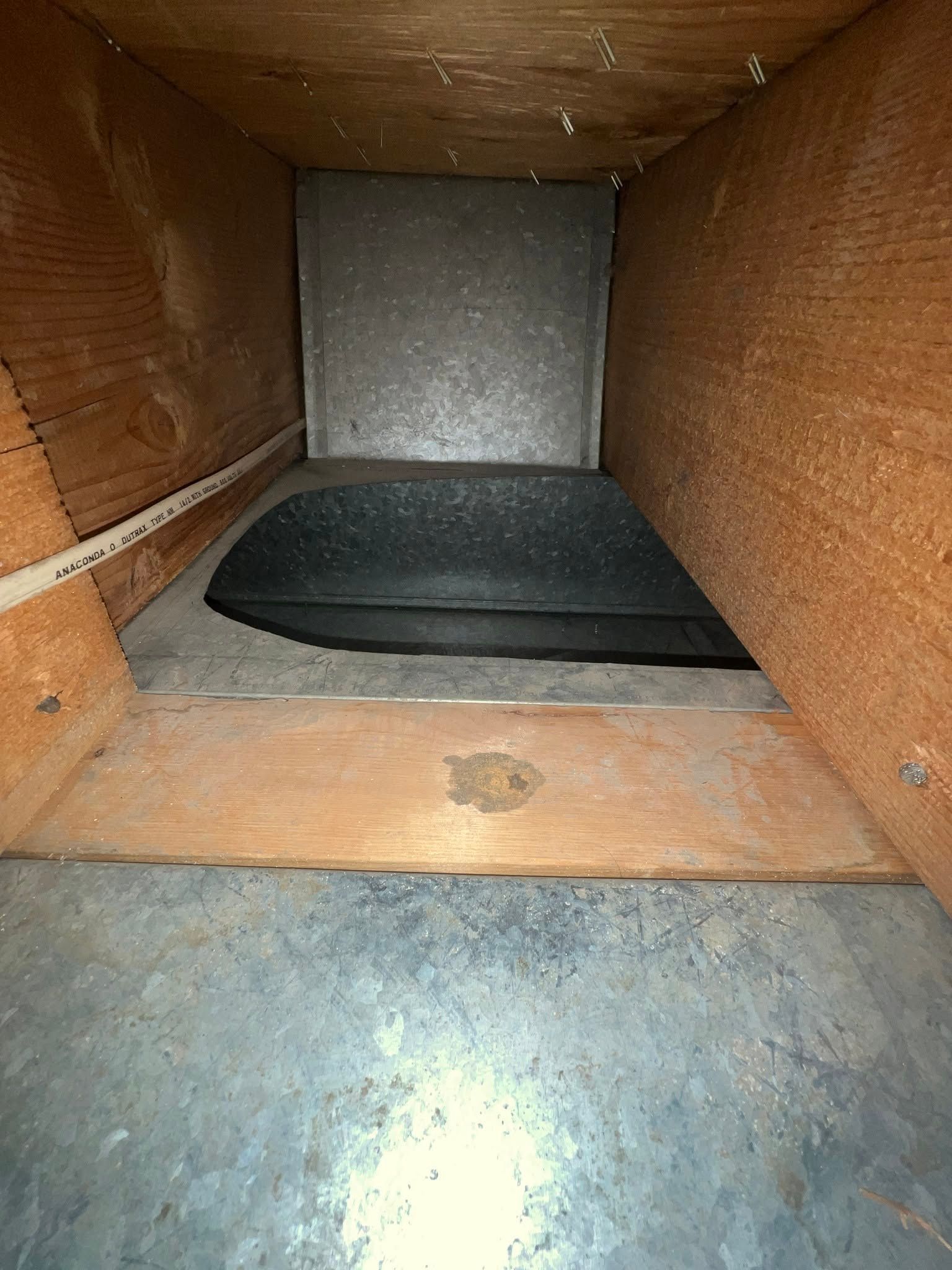 Inside a wooden duct, a dark black pad rests on the floor against a silver back panel.