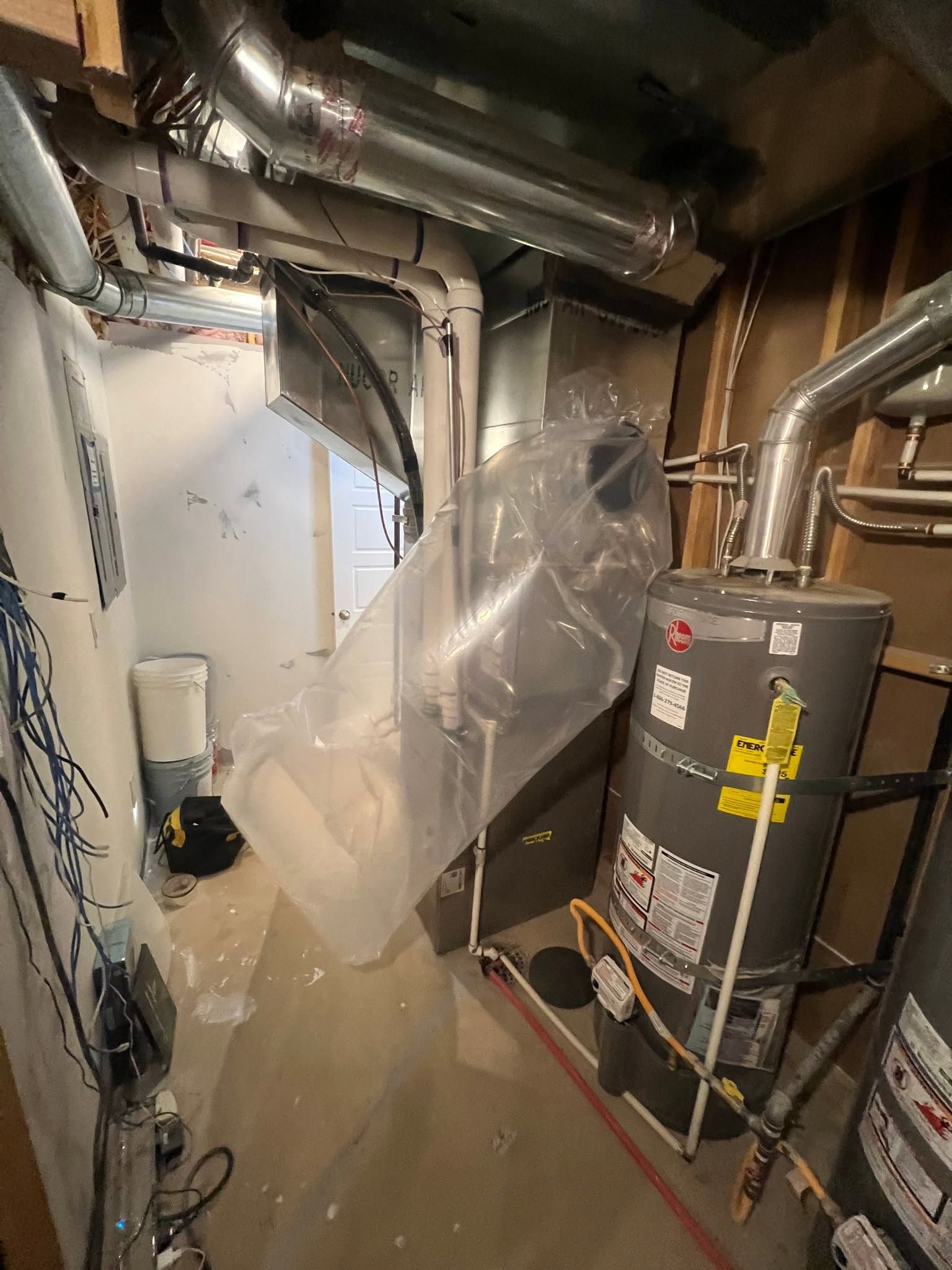 Basement utility room with HVAC ducts, water heater, and a plastic-covered walkway.