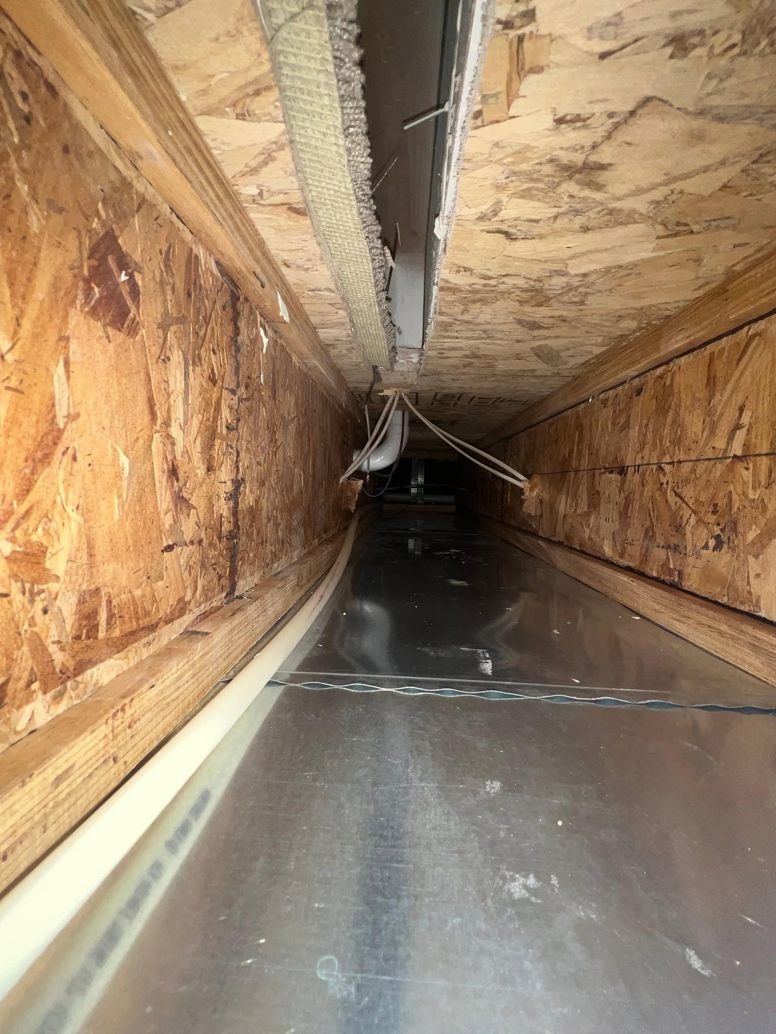 Long, narrow corridor with plywood walls, a dark floor, and a damaged ceiling panel hanging overhead