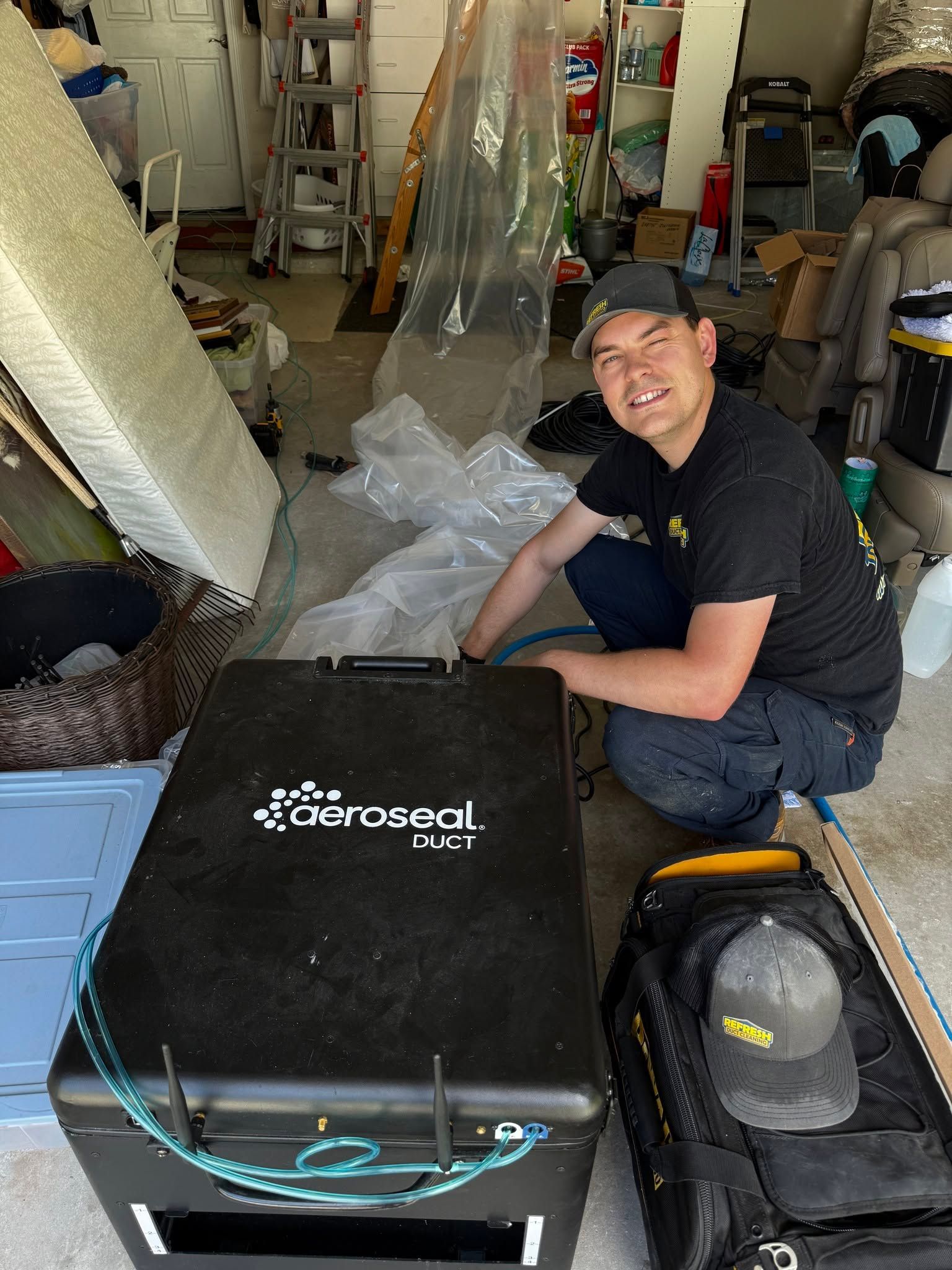 Man sitting beside a black Aeroseal box in a workshop, with tools and packing materials around him