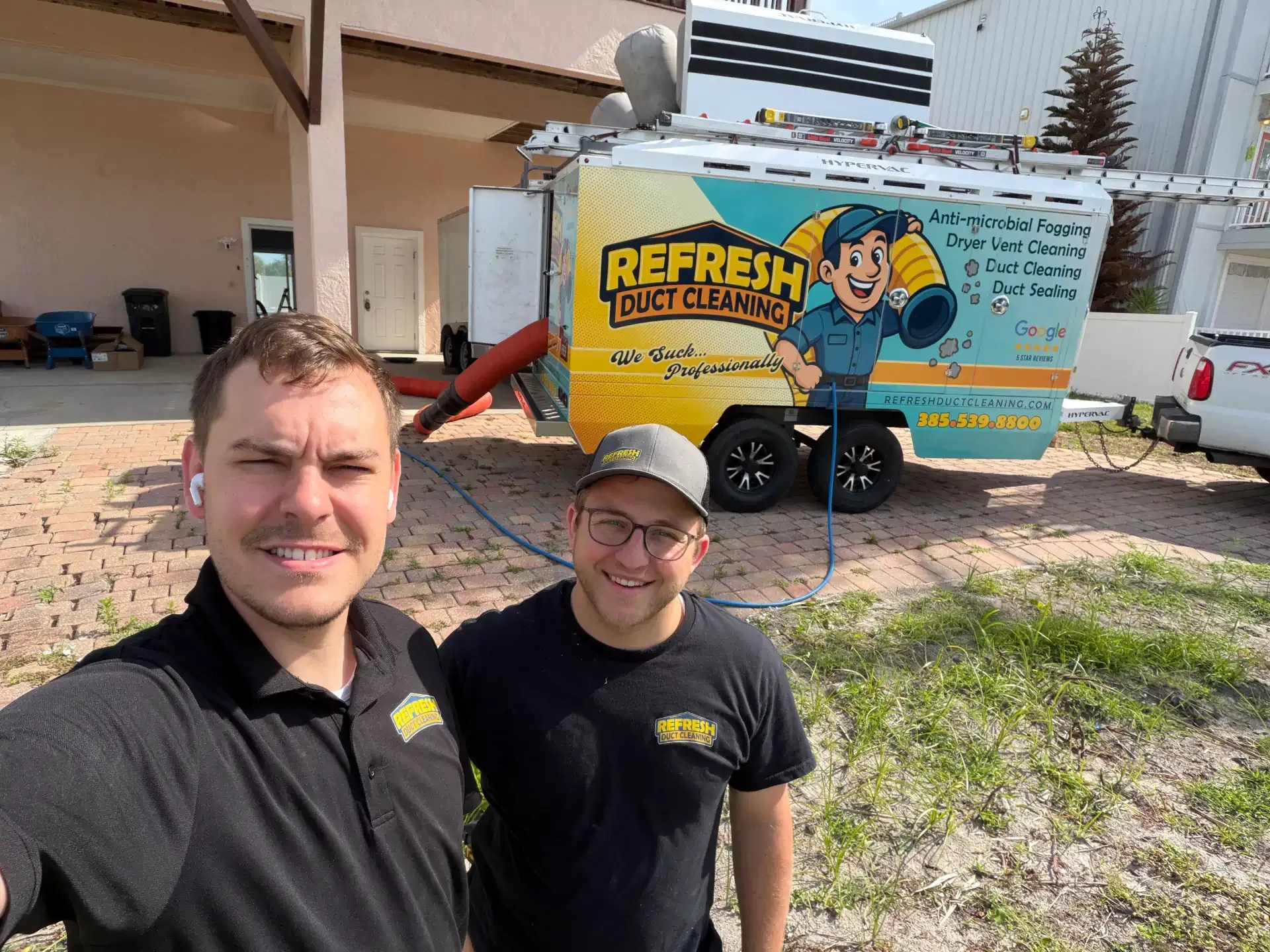 Two men in black shirts posing beside a colorful REFRESH truck in a driveway