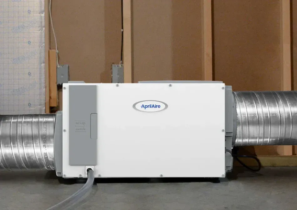 White HVAC ventilation unit connected to large silver ducts in an indoor utility room