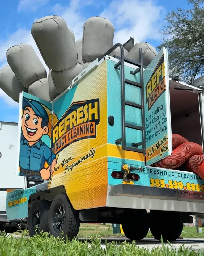 Fresh Cleaning truck with cartoon mascot, large gray cushions on top, parked outdoors under blue sky