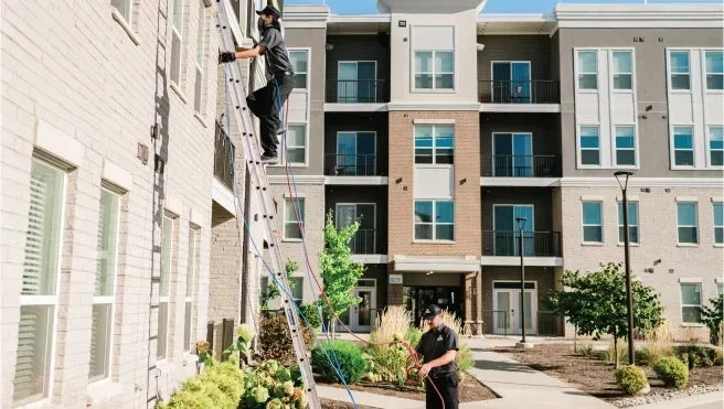 Modern apartment courtyard with a person watering plants between multi-story buildings.