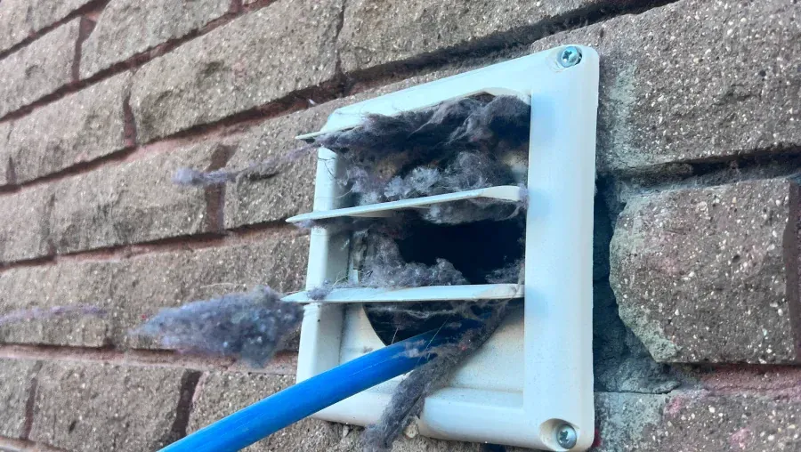 Blue cable entering a wall vent filled with gray insulation fibers against a brick wall.