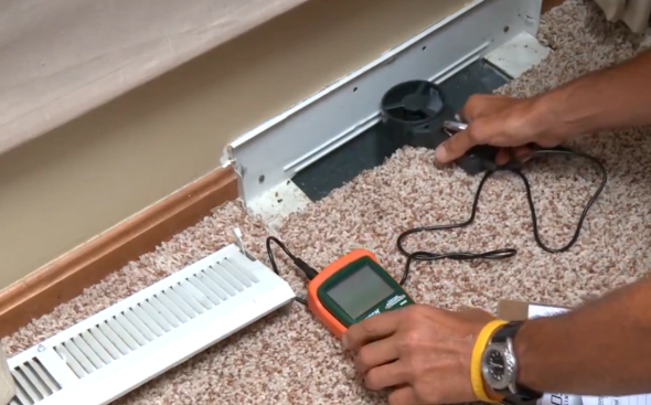 Technician testing electrical outlet wiring under a baseboard with a multimeter