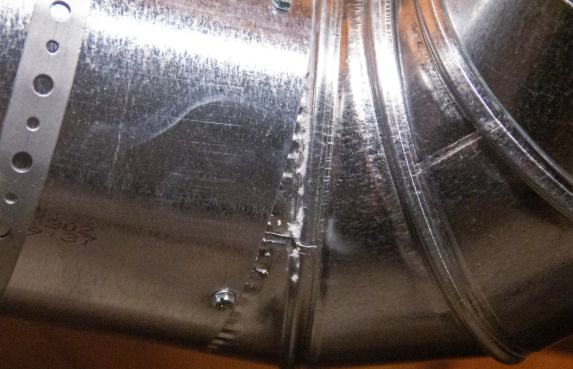 Close-up of a shiny metal pipe joint with rivets and weld seams showing small drips or corrosion marks