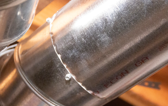 Close-up of a shiny metal pipe with a jagged crack or cut seam