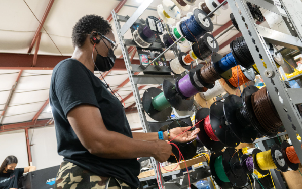 Person wearing a mask browses colorful spools of filament in a 3D printing supply aisle