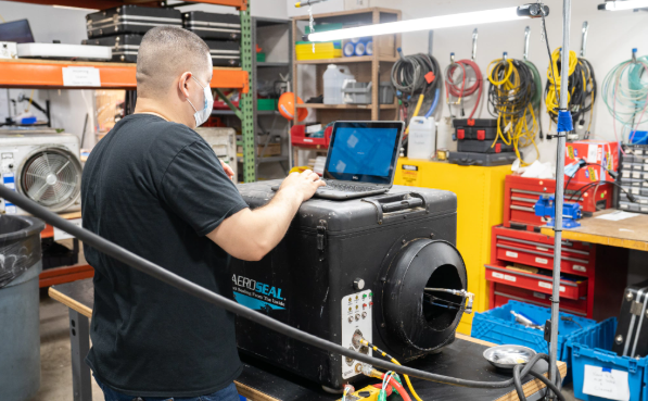 Technician using a laptop on a machine in a workshop with tools and cables nearby