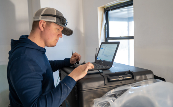 Person using a laptop beside a plastic-covered workbench in a bright room