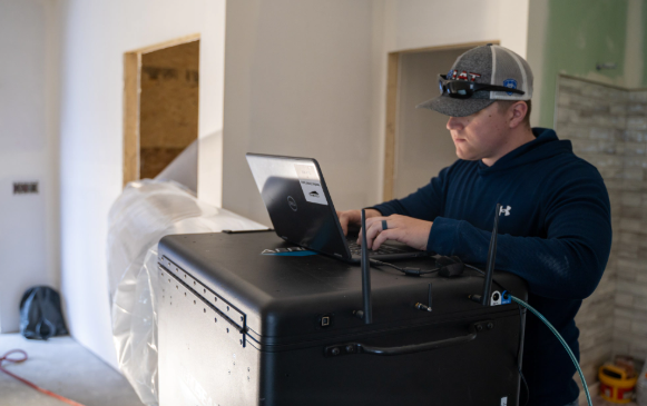 Person using a laptop beside a large black equipment case in a room under renovation.