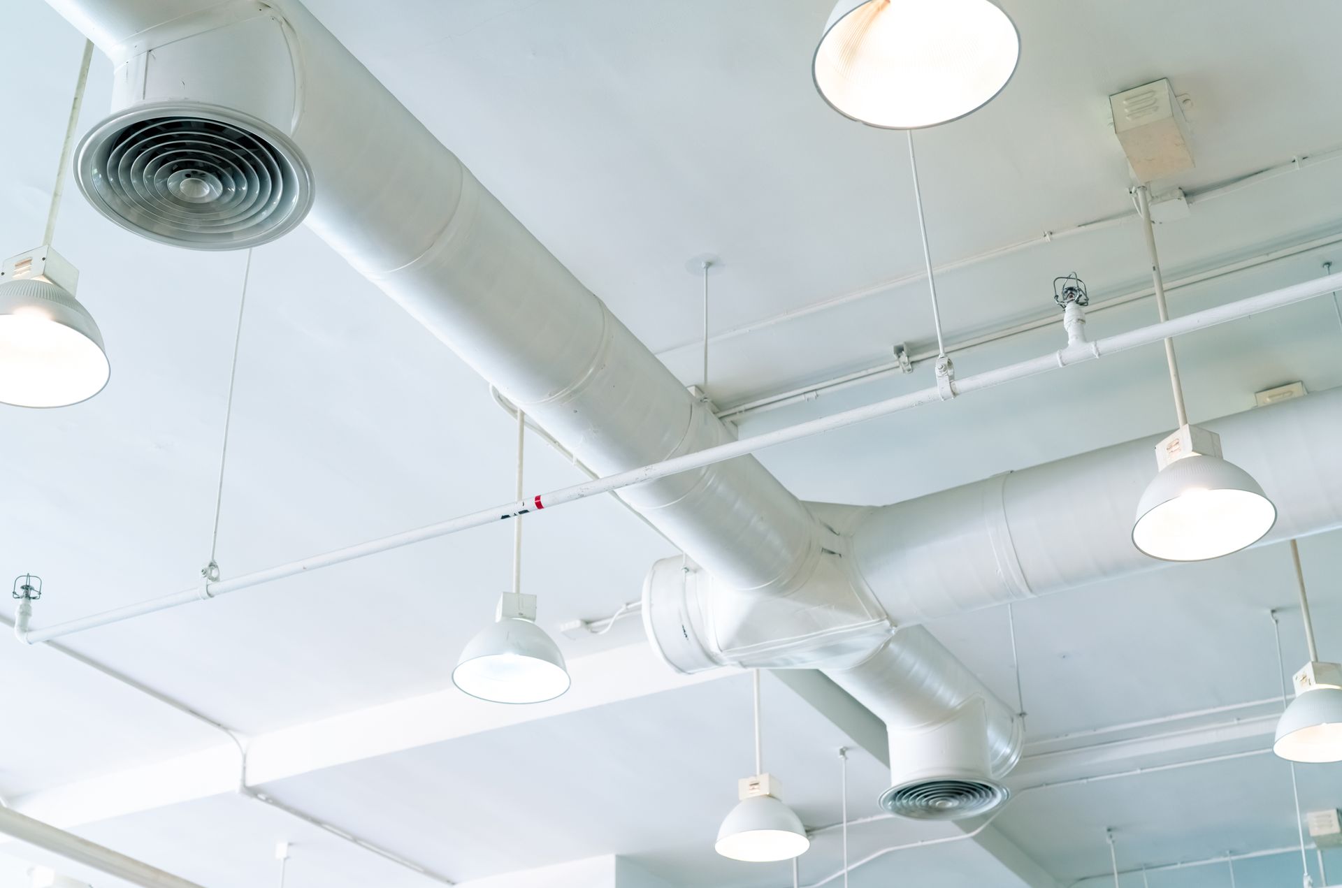 White industrial ceiling with exposed ducts and hanging pendant lights