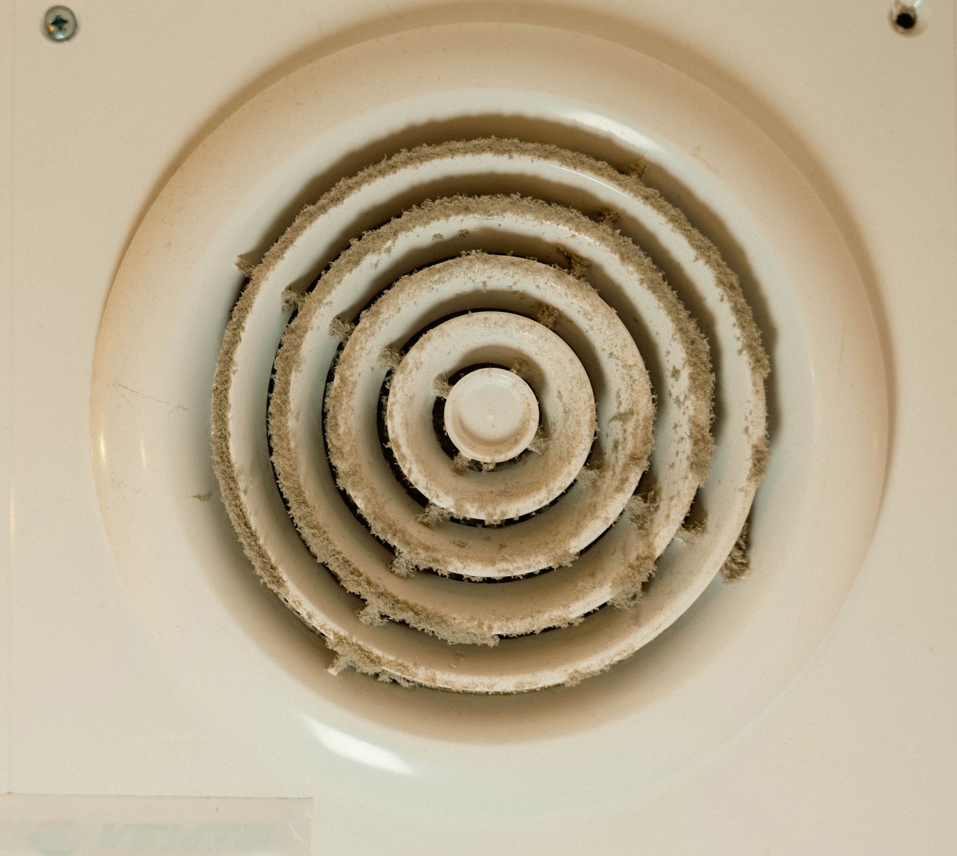 Dusty white ventilation fan grille on a beige ceiling.