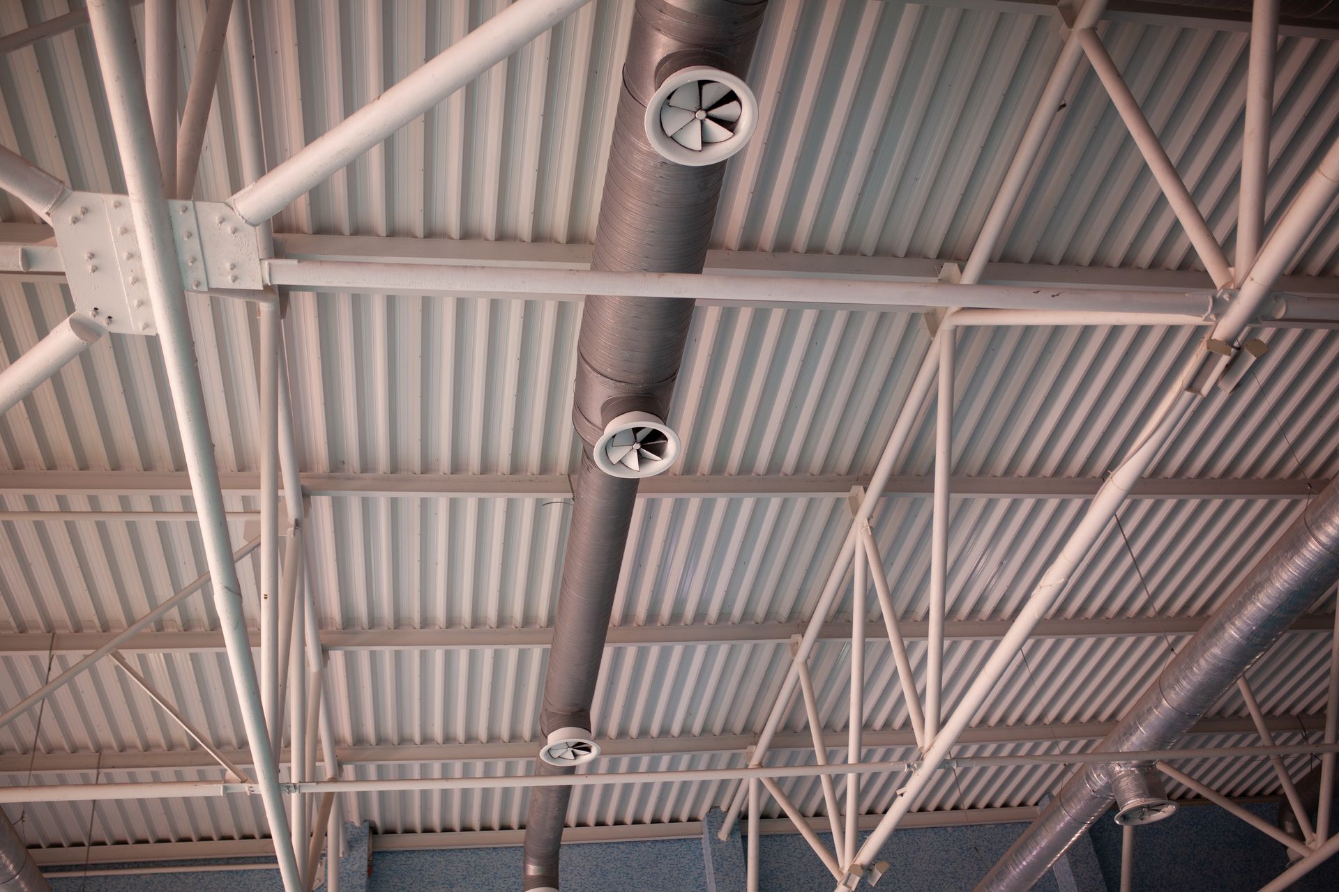 Ceiling with exposed metal beams and three industrial fans in a warehouse-like interior
